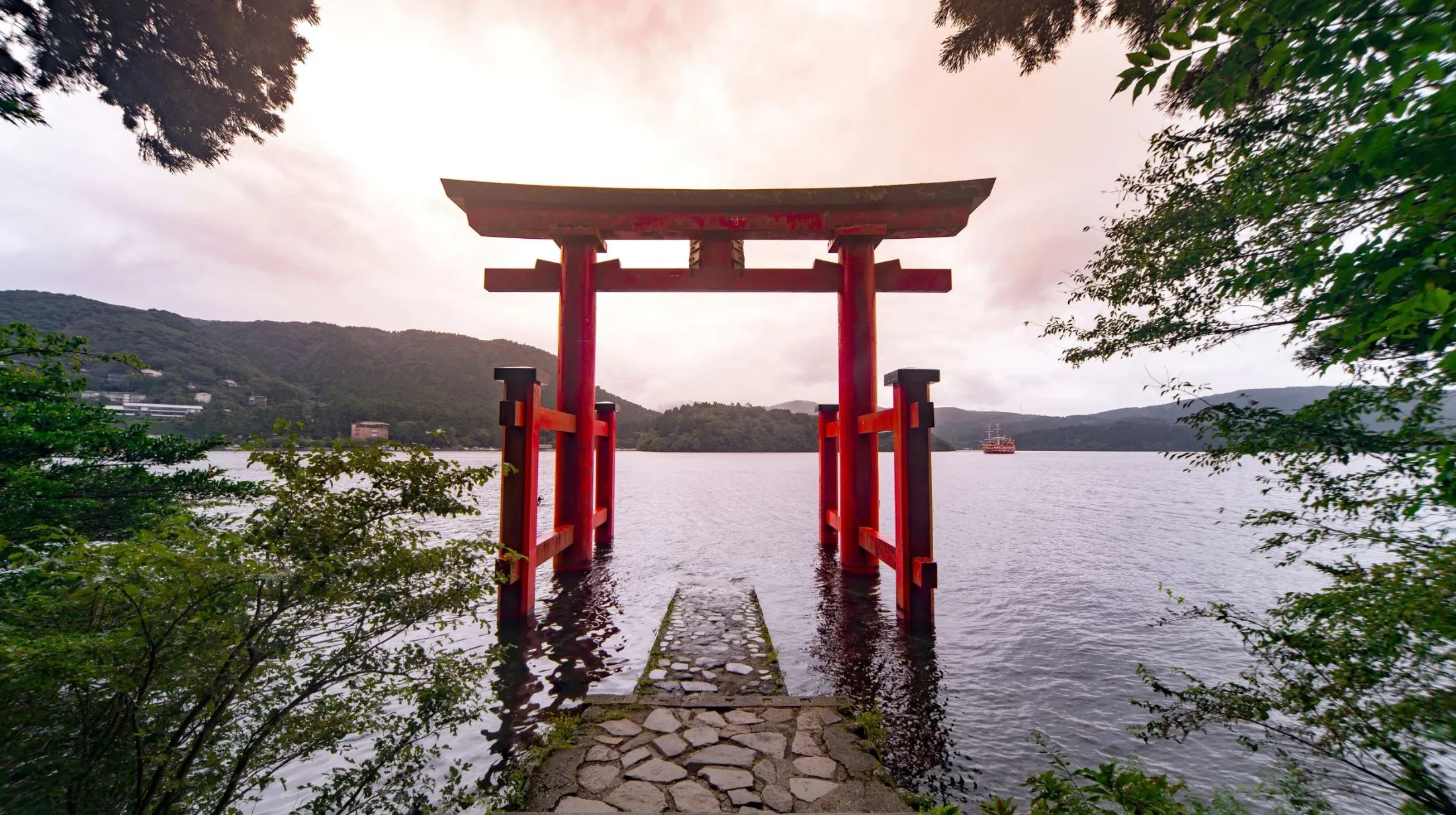 Torii rouge traditionnel du sanctuaire Hakone sur le lac Ashi, avec montagnes et bateau au Japon