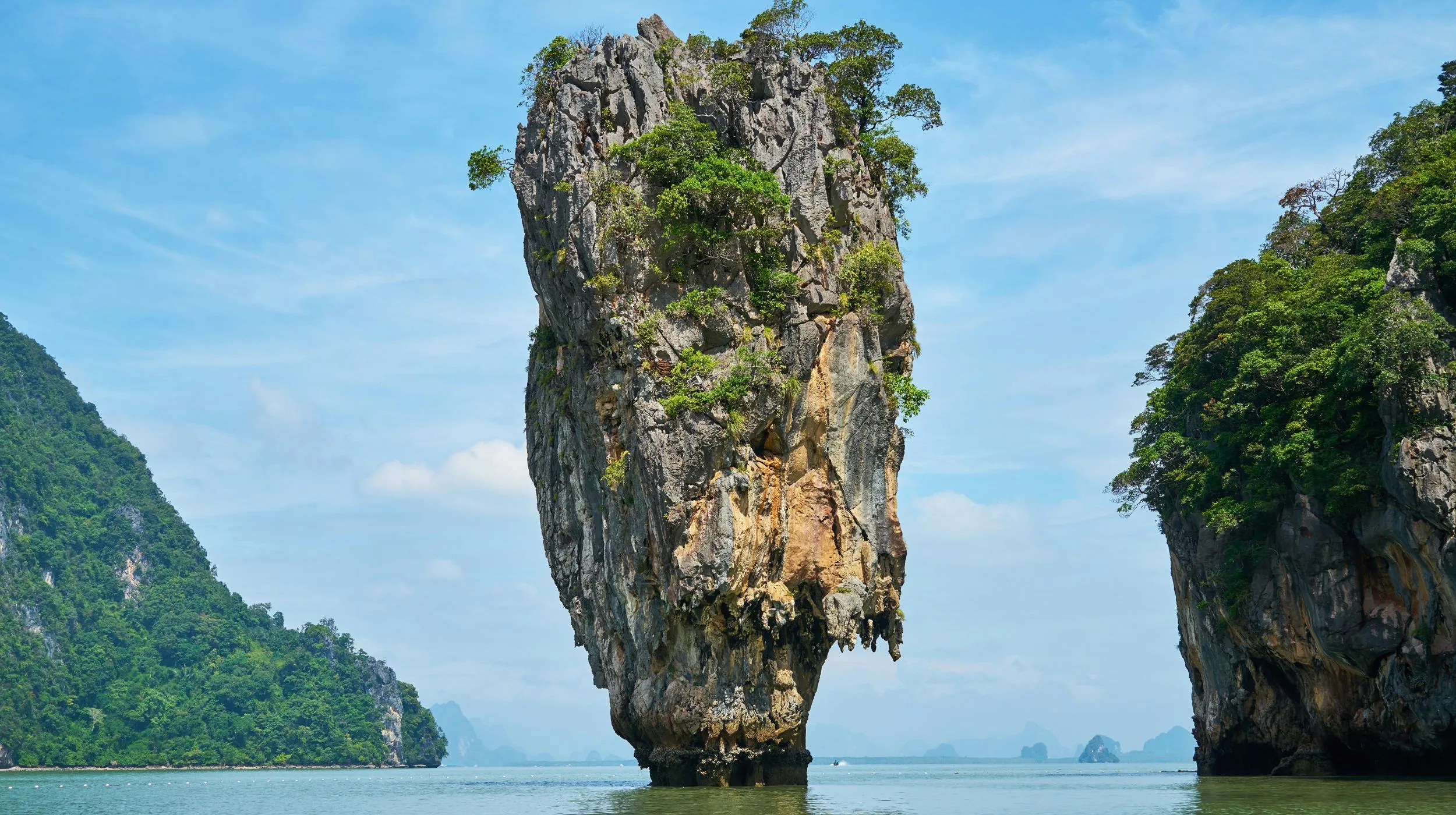 Un rocher majestueux émerge des eaux calmes, entouré de collines verdoyantes.