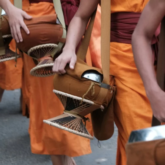 Des moines en robes orange défilent, portant des bols rituels, dans une scène culturelle vibrante.