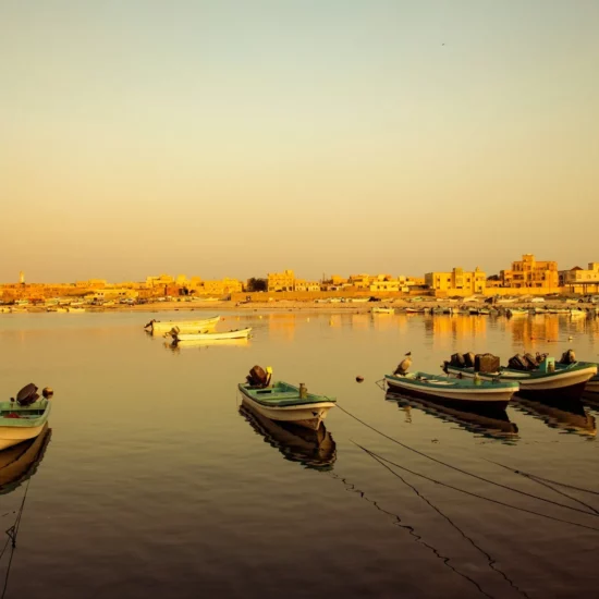 Bateaux colorés amarrés dans une eau calme, illuminés par la lumière dorée du coucher de soleil.
