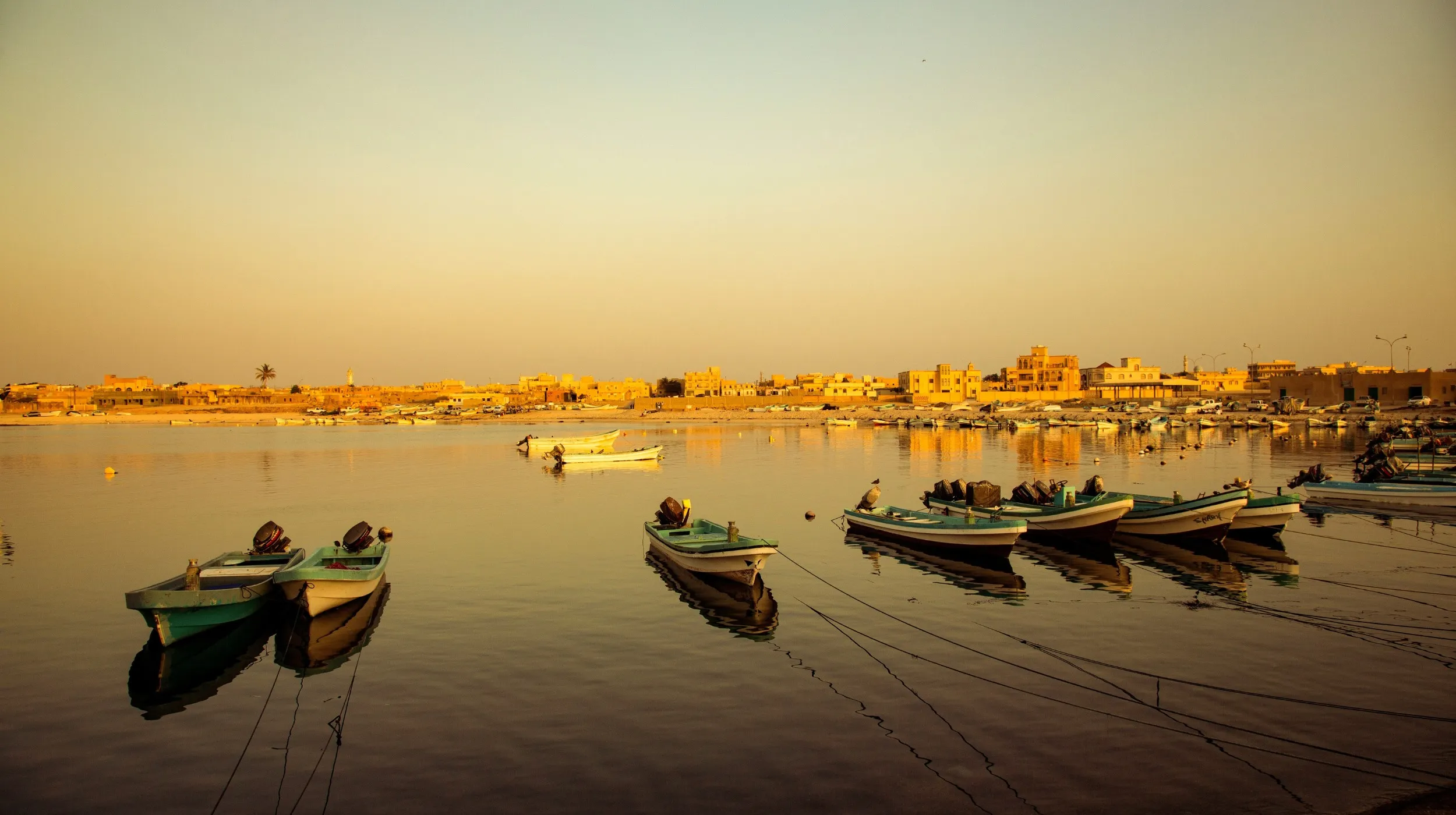 Port paisible de Salalah à Oman avec des bateaux colorés et un coucher de soleil éclatant, créant une ambiance magique.
