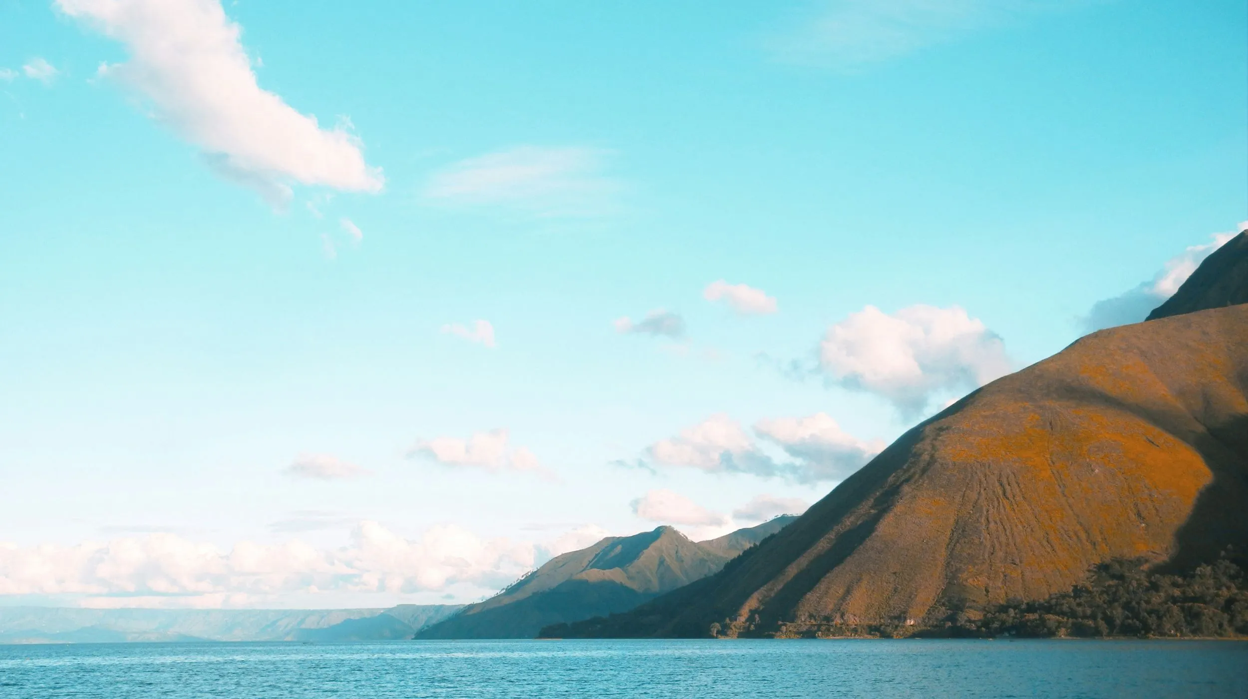Lac paisible entouré de montagnes majestueuses sous un ciel lumineux et parsemé de nuages.