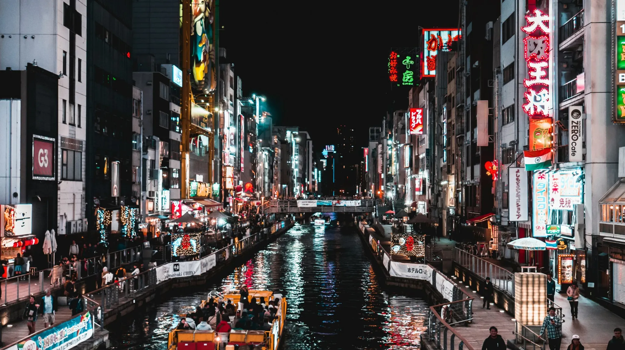 Ville animée la nuit, illuminée par des néons colorés et bordée d'un canal scintillant.
