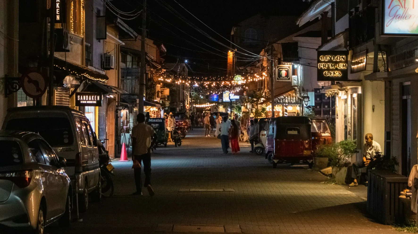 Rue animée à la tombée de la nuit, illuminée par des guirlandes à l'ambiance conviviale.
