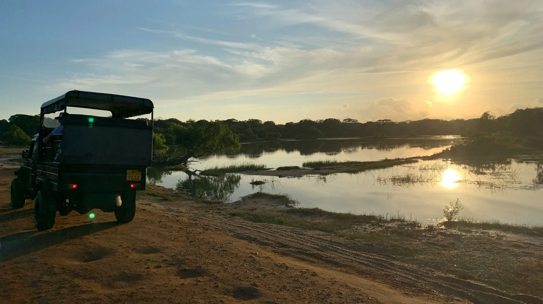 Coucher de soleil sur un paisible plan d'eau, avec un véhicule garé sur une route de terre.