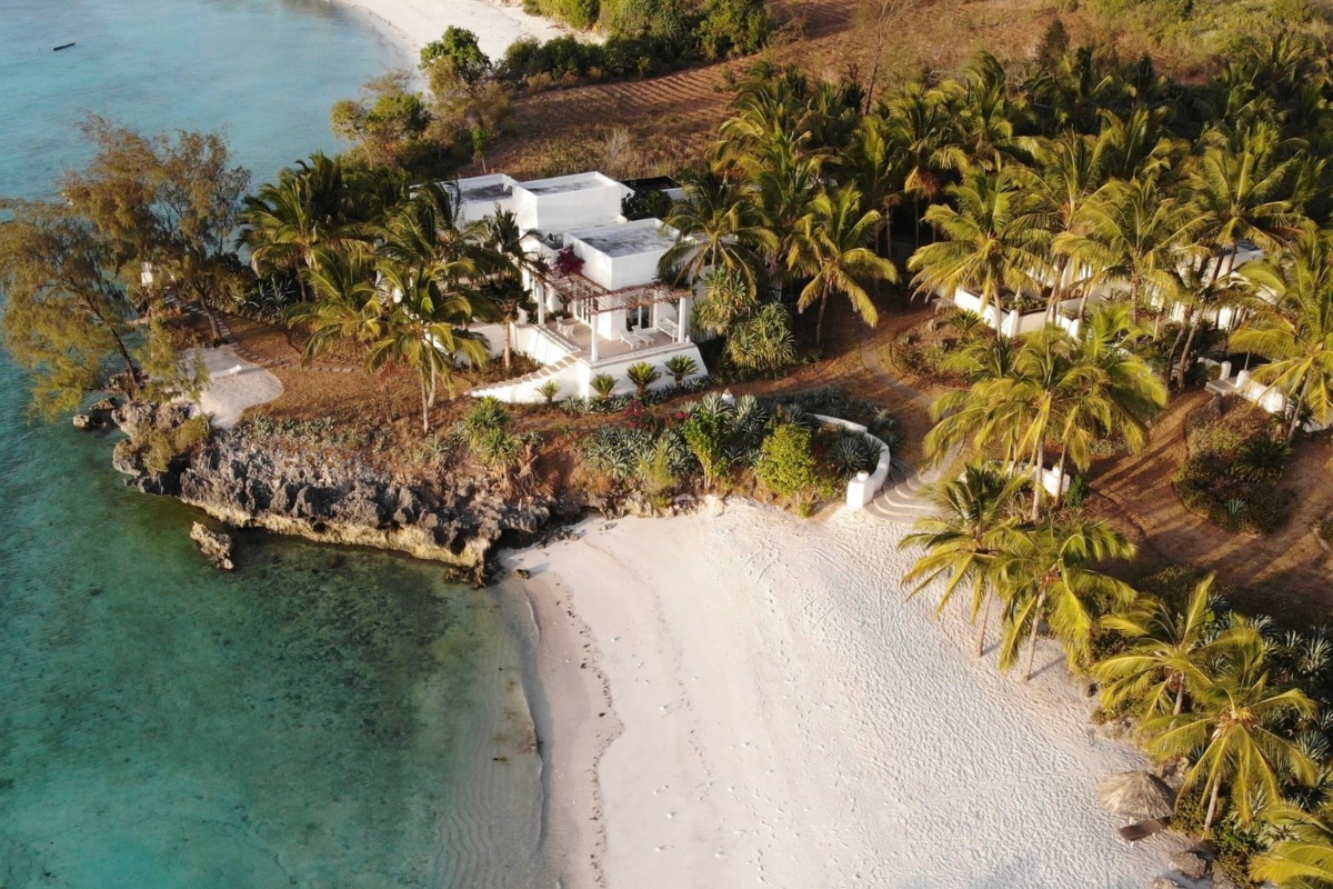 Plage paradisiaque bordée de palmiers, avec une villa blanche surplombant des eaux turquoise.