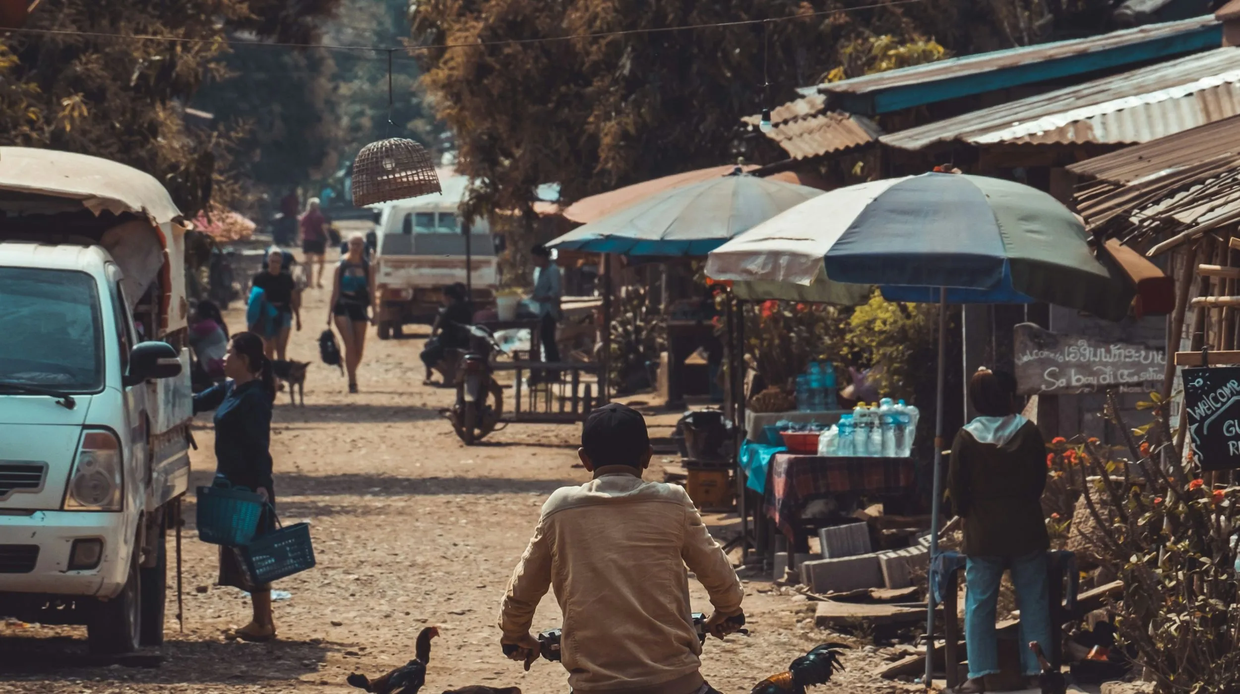 Scène animée d'un marché local avec des étals colorés et des personnes en mouvement dans une ambiance conviviale.