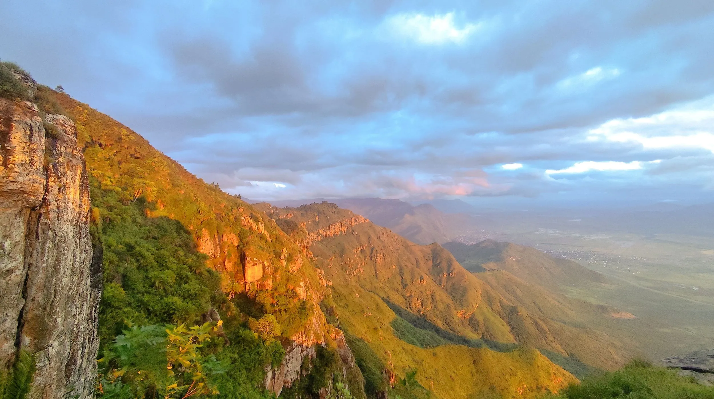 Paysage montagneux époustouflant au coucher du soleil, avec des collines verdoyantes et un ciel nuageux.