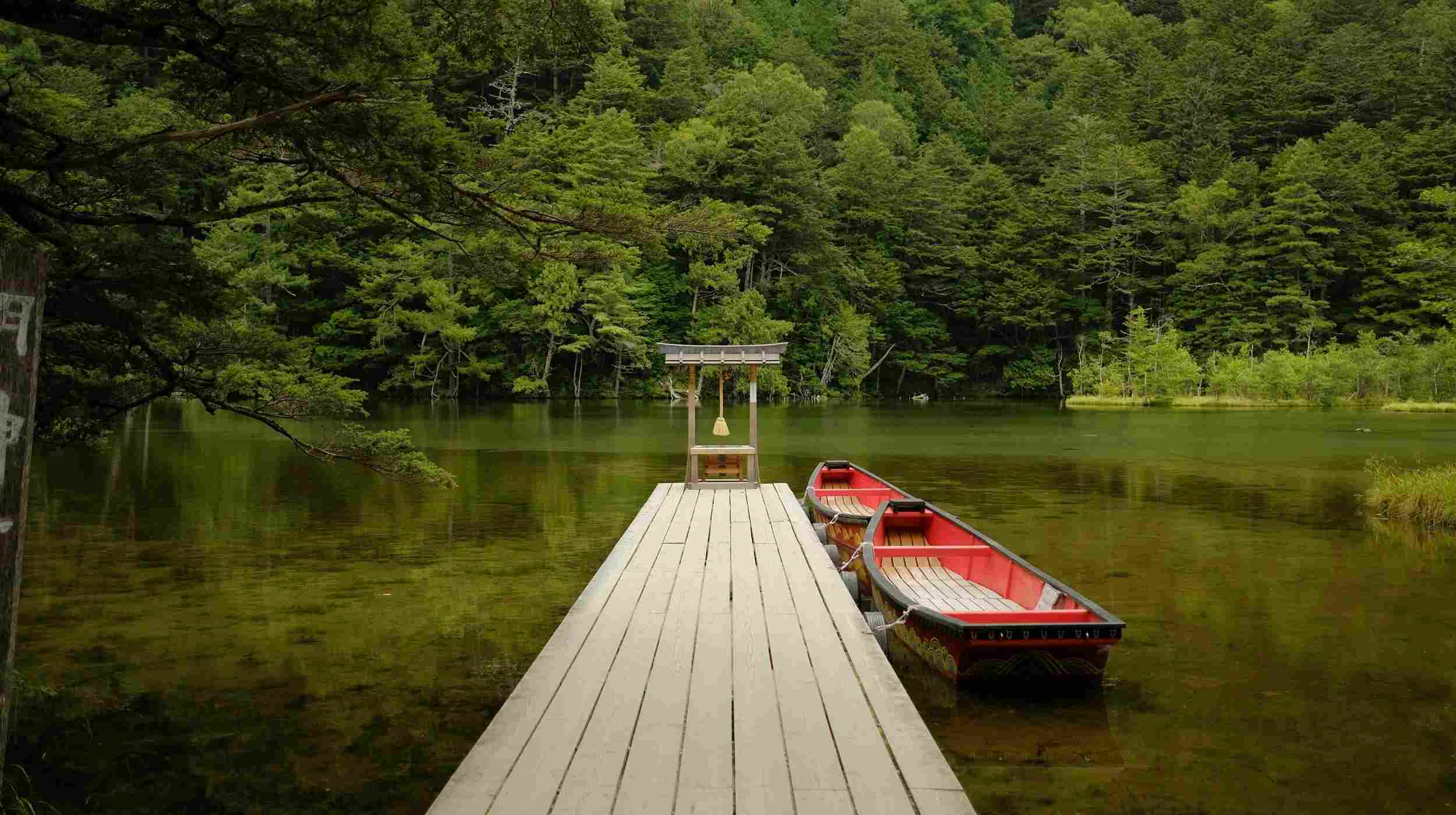 Lac paisible à Kamikochi au Japon avec torii et barque traditionnelle, entouré de forêt – destination nature et détente au Japon